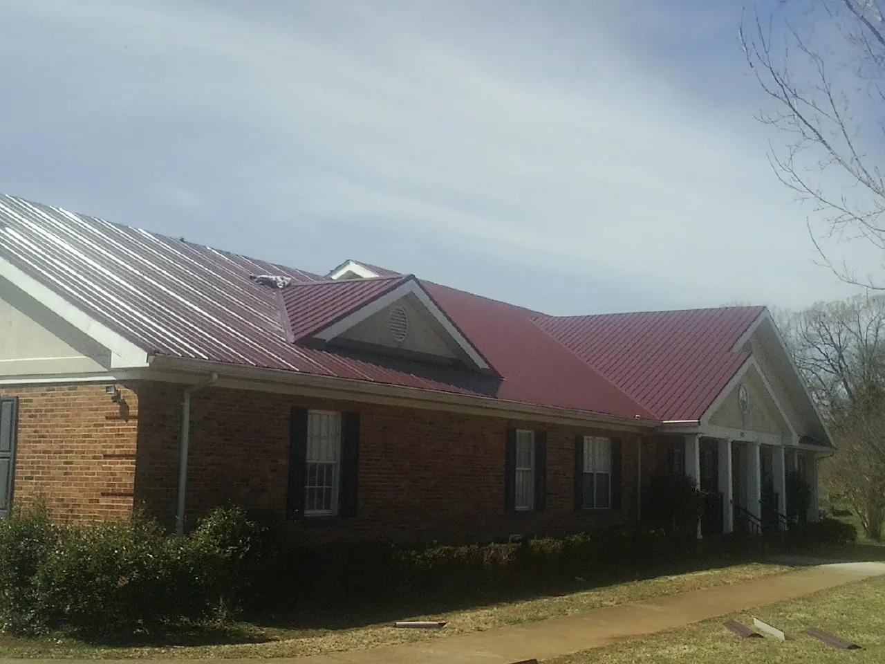 Red metal roof with gabled entries on a long brick building, from a Hail Damage Roof Repair job in West Frankfort