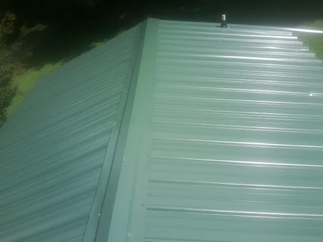 New green metal panels meeting at the ridge of a roof — Flat Roof Repair work by our crew in West Frankfort