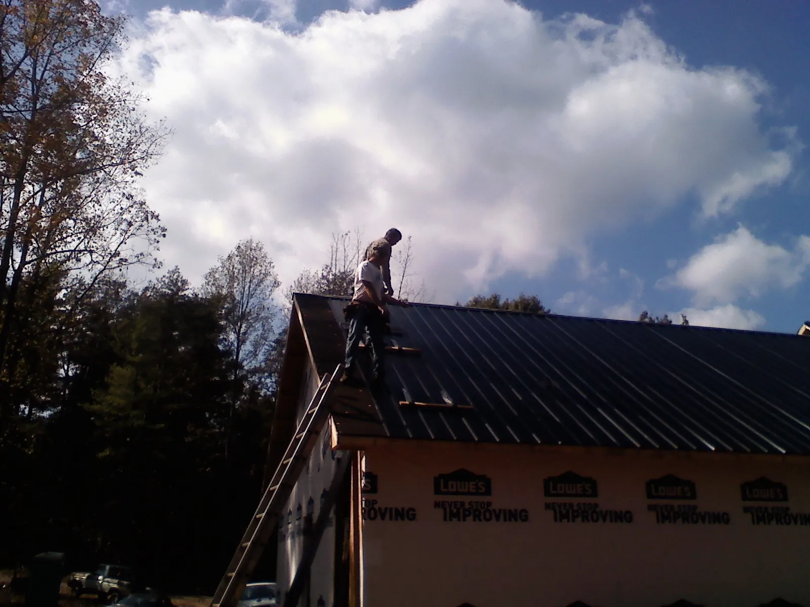 Roofer fastening dark metal panels high against a cloudy sky, from a Roof Inspection job in West Frankfort