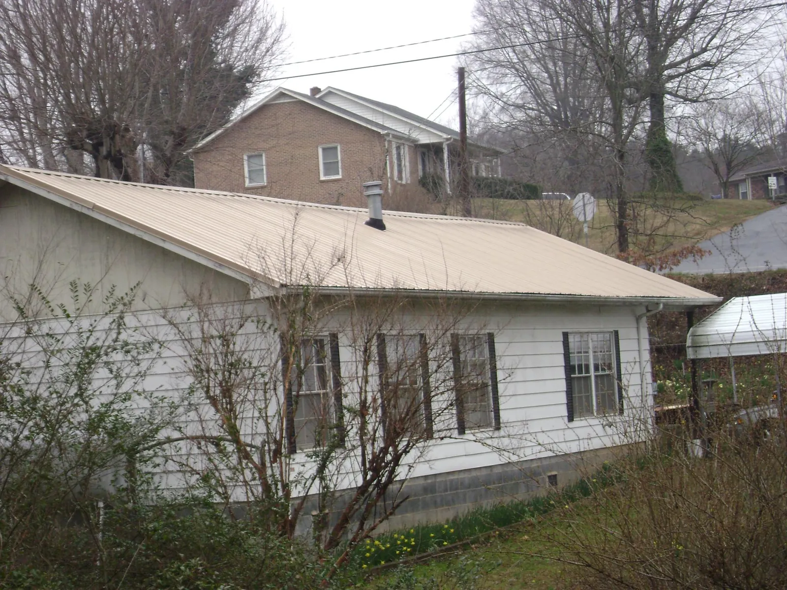 Tan metal roof on a white sided house set into a hillside — Commercial Roofing by Roofing Brothers in West Frankfort